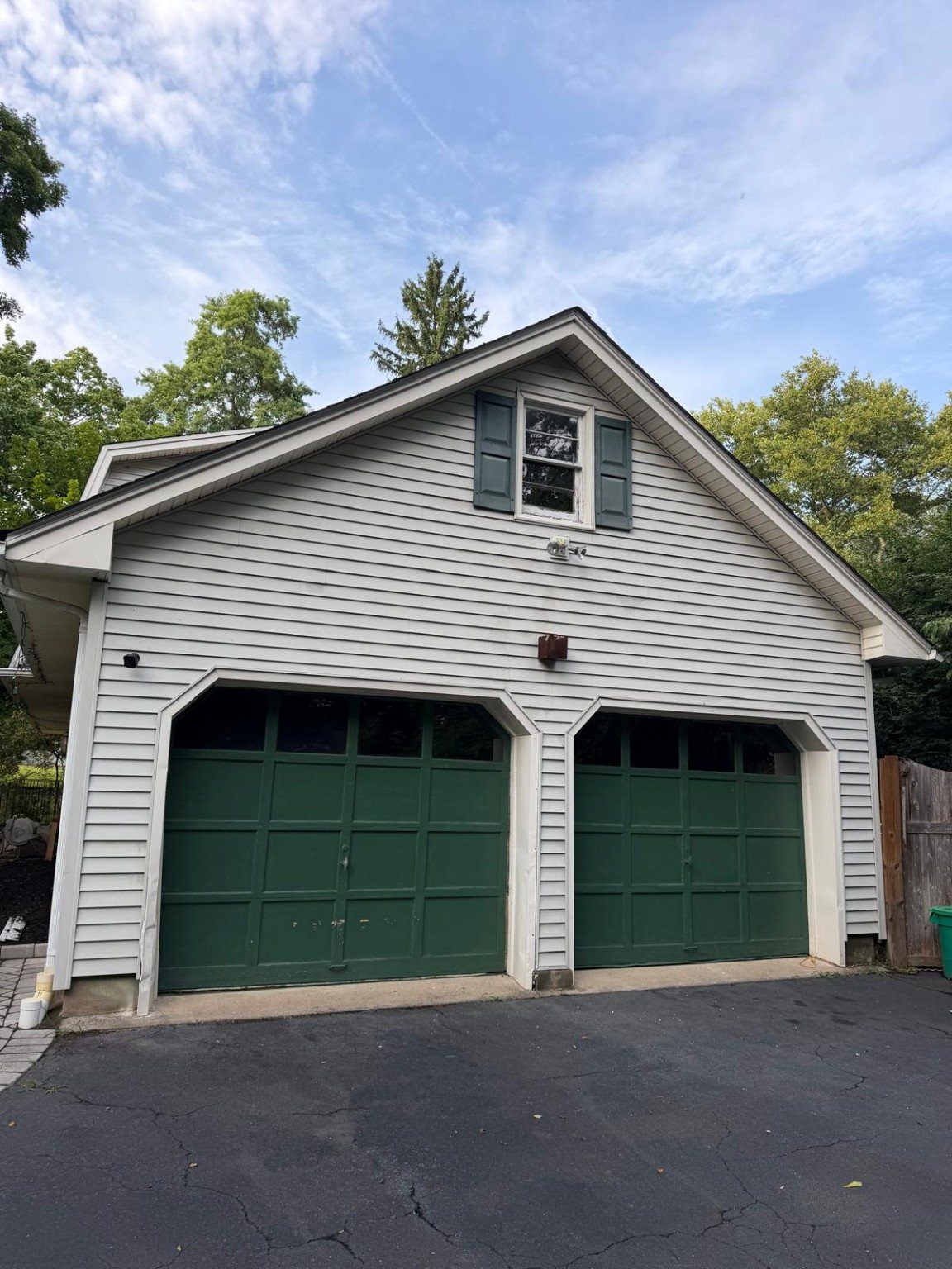 Clean garage exterior with light siding and two green garage doors.