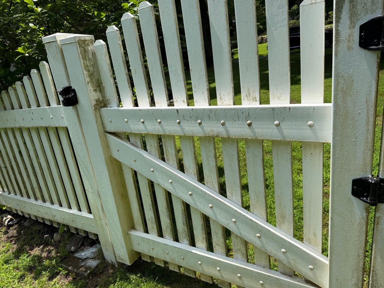 Close view of a white vinyl gate before cleaning with visible organic staining.