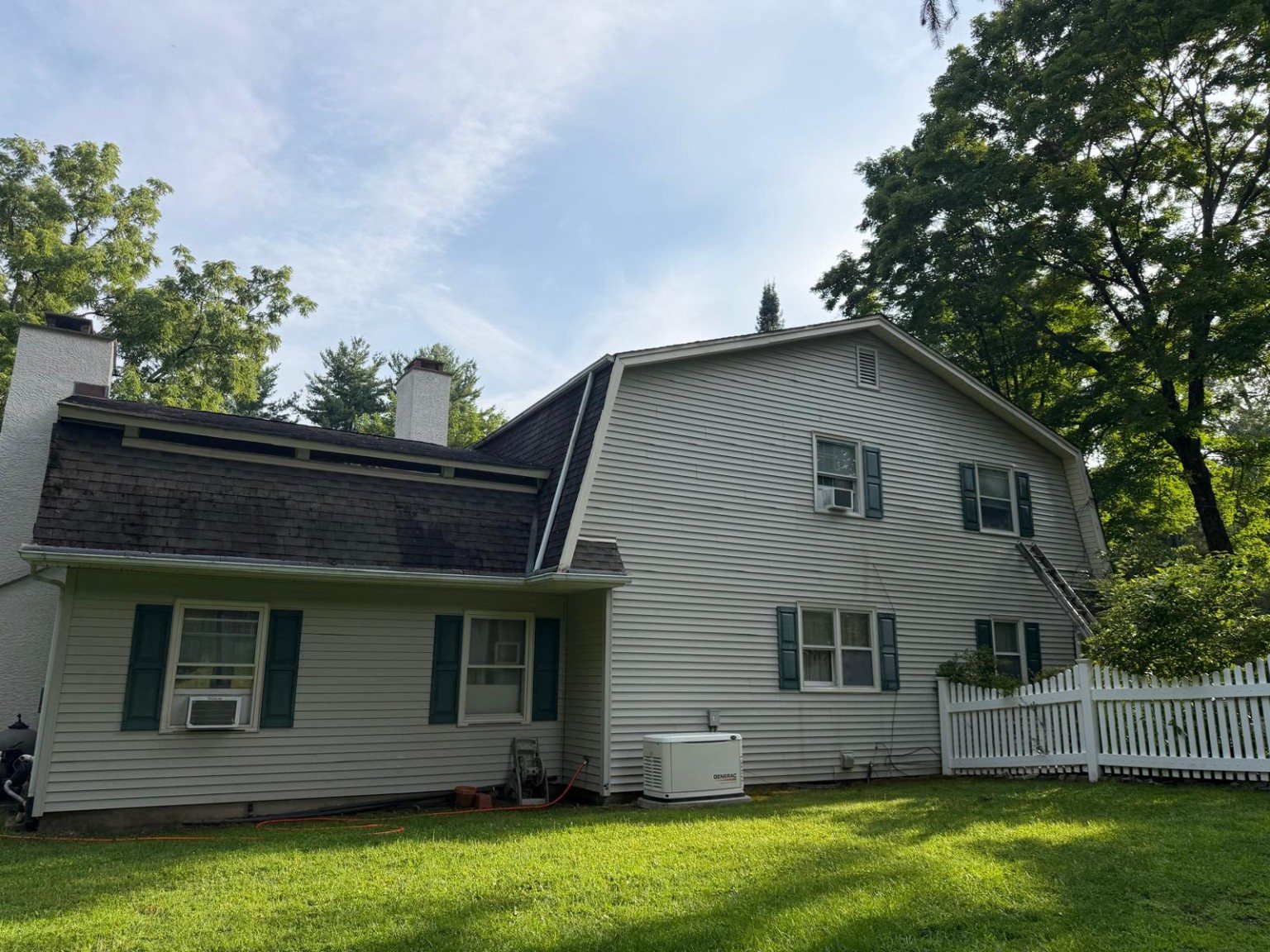 Clean rear exterior of a light-colored home with white fencing and a green lawn.