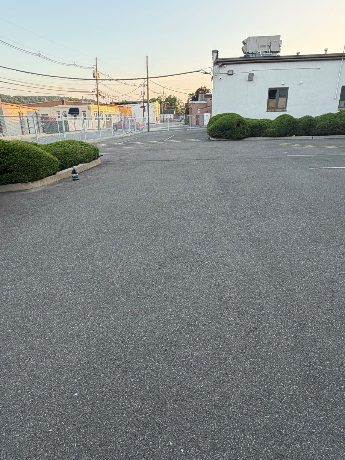 Wide commercial parking area before surface work with a lighter weathered pavement appearance.