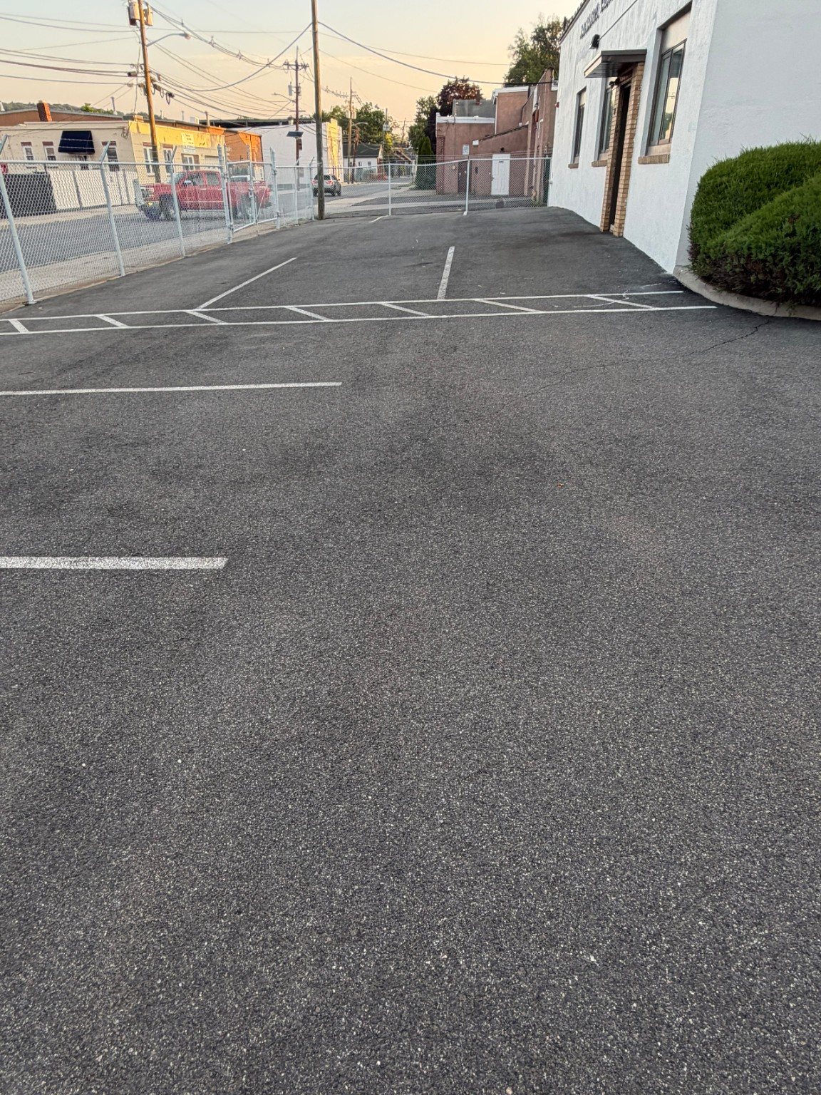 Commercial parking spaces before surface work near a fenced property edge.