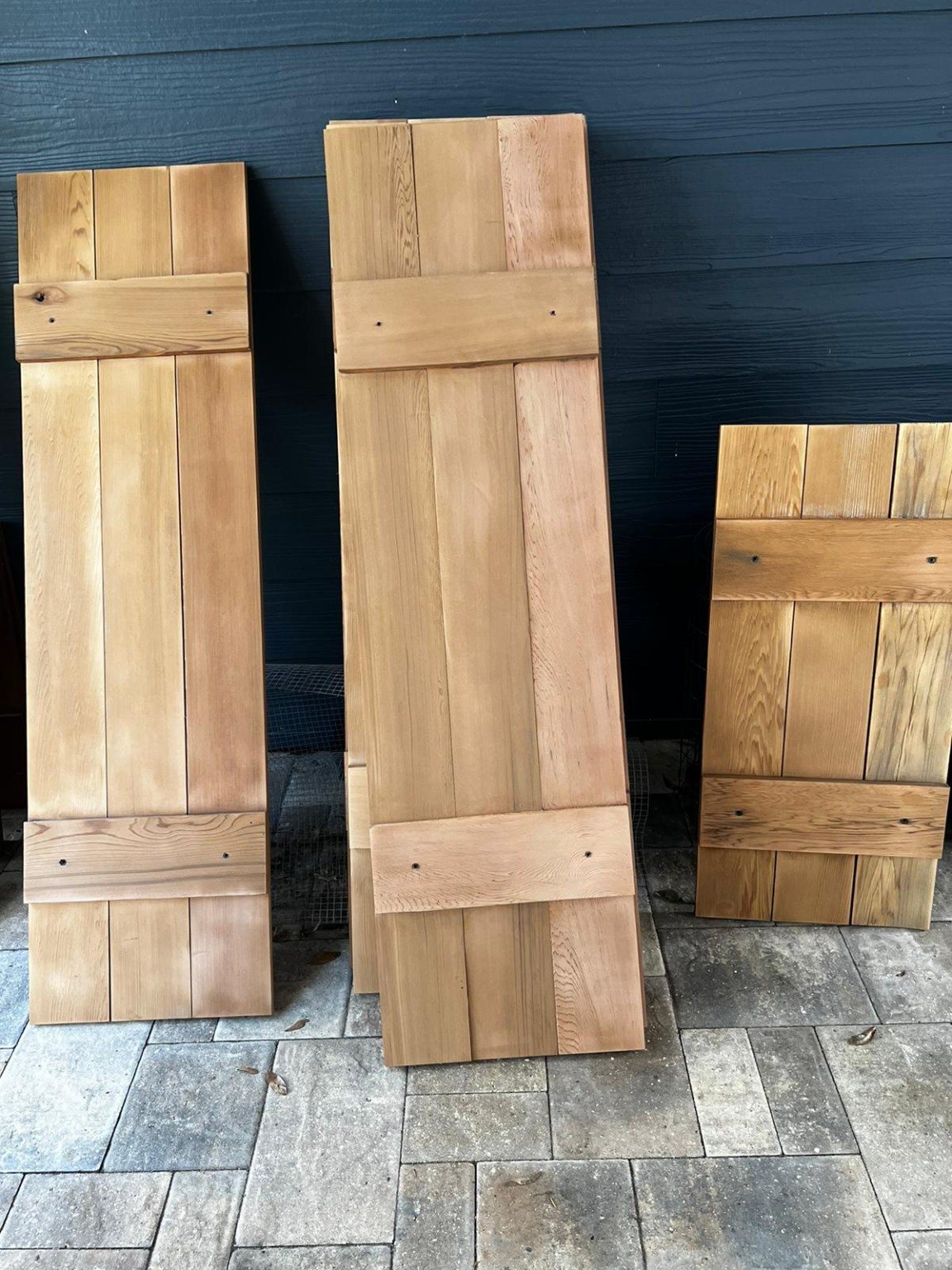 Unfinished cedar shutters leaning against the exterior wall before their final finish and installation.